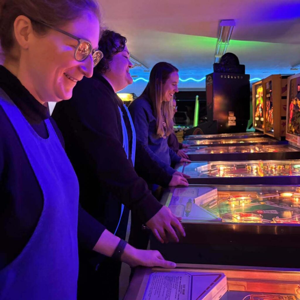 A line of pinball tables all being played by belles and chimes members
