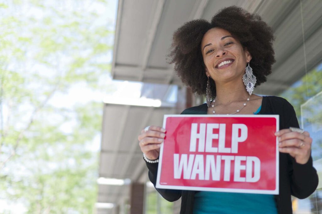 a woman holding a help wanted sign